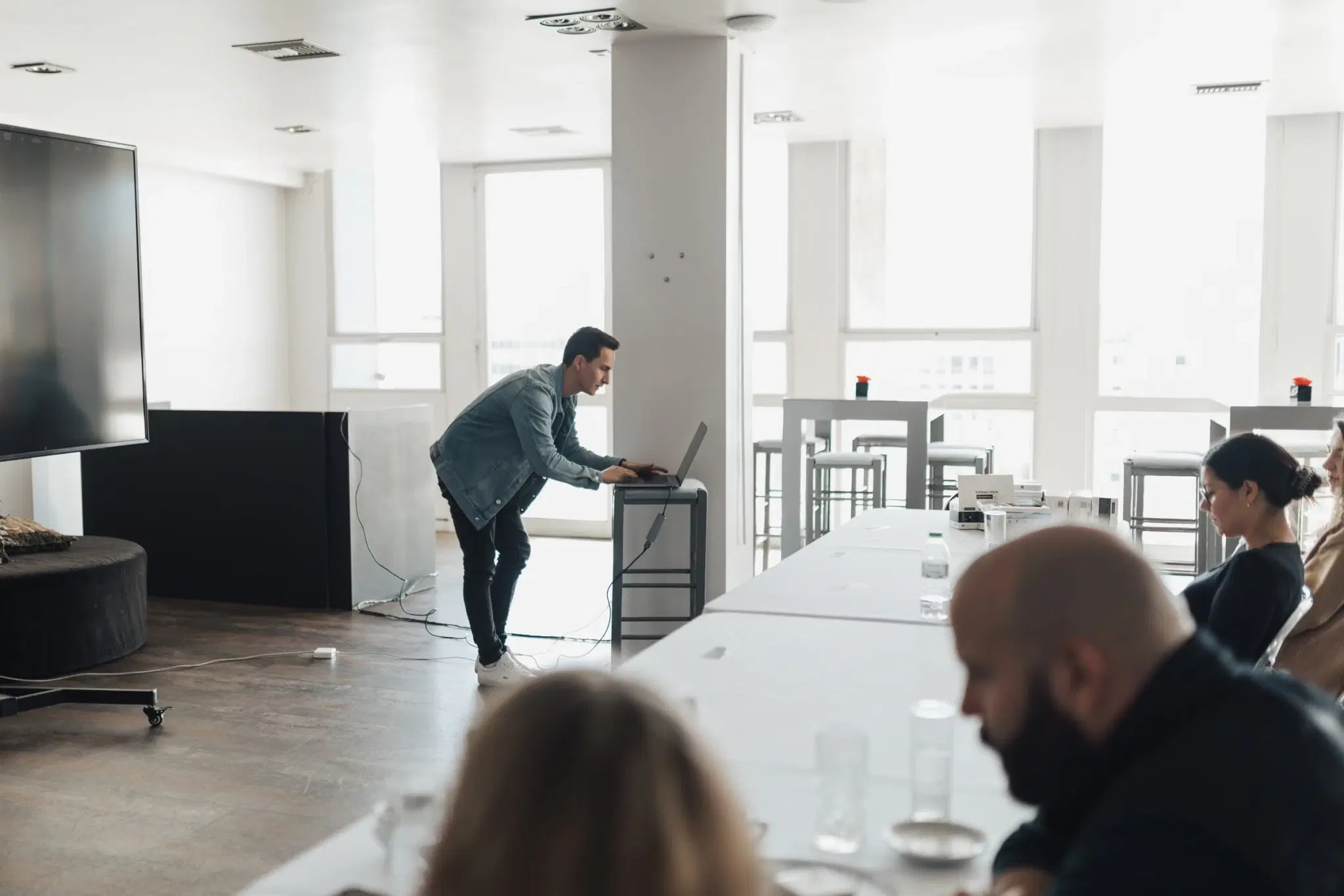 A facilitator standing at a laptop at the front of a light meeting room.
